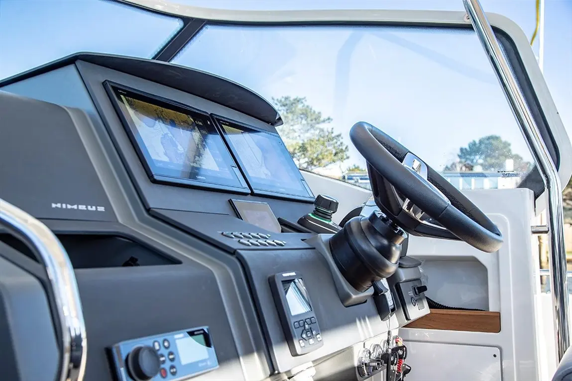 Nimble boat dashboard featuring dual screens displaying maps, a steering wheel, and navigation controls in a sunlit cabin.